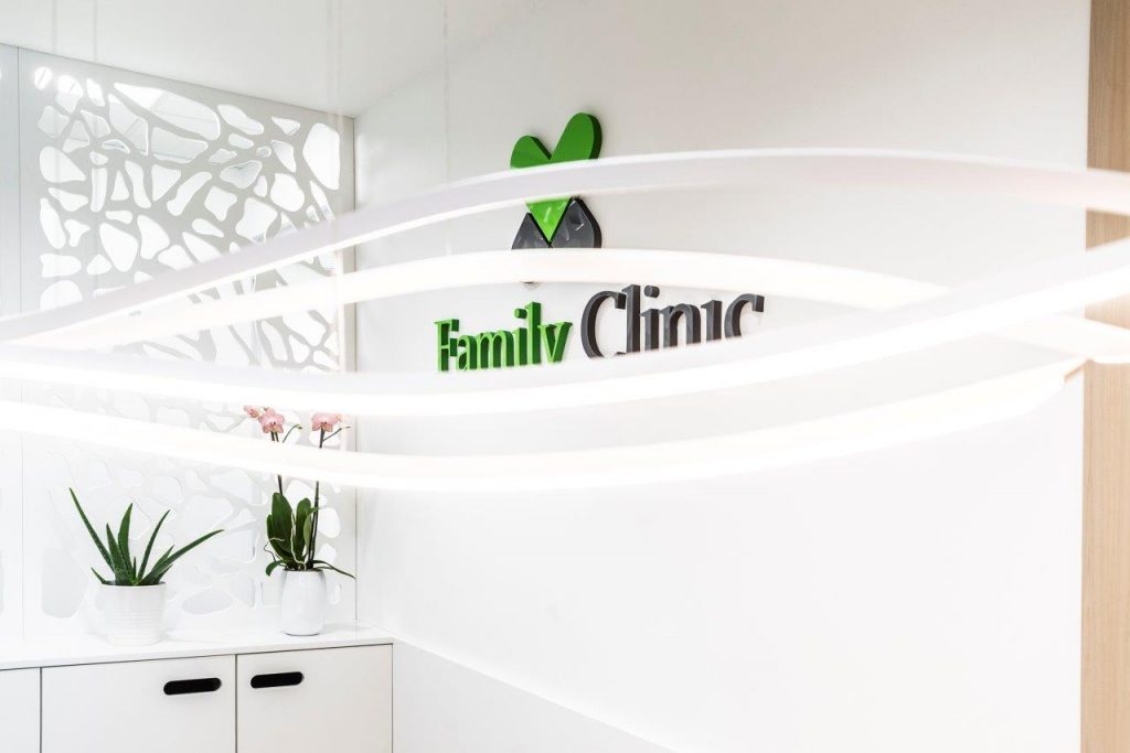 zielone logo Family Clinic na białej ścianie obok dwóch kwiatków